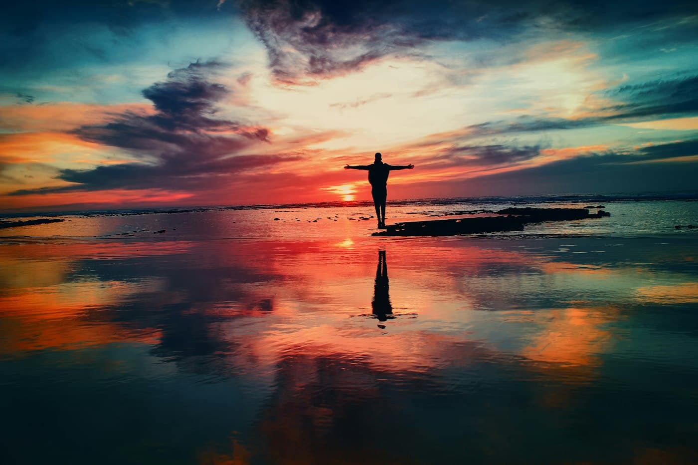 A lone figure with arms outstretched in worship at sunrise